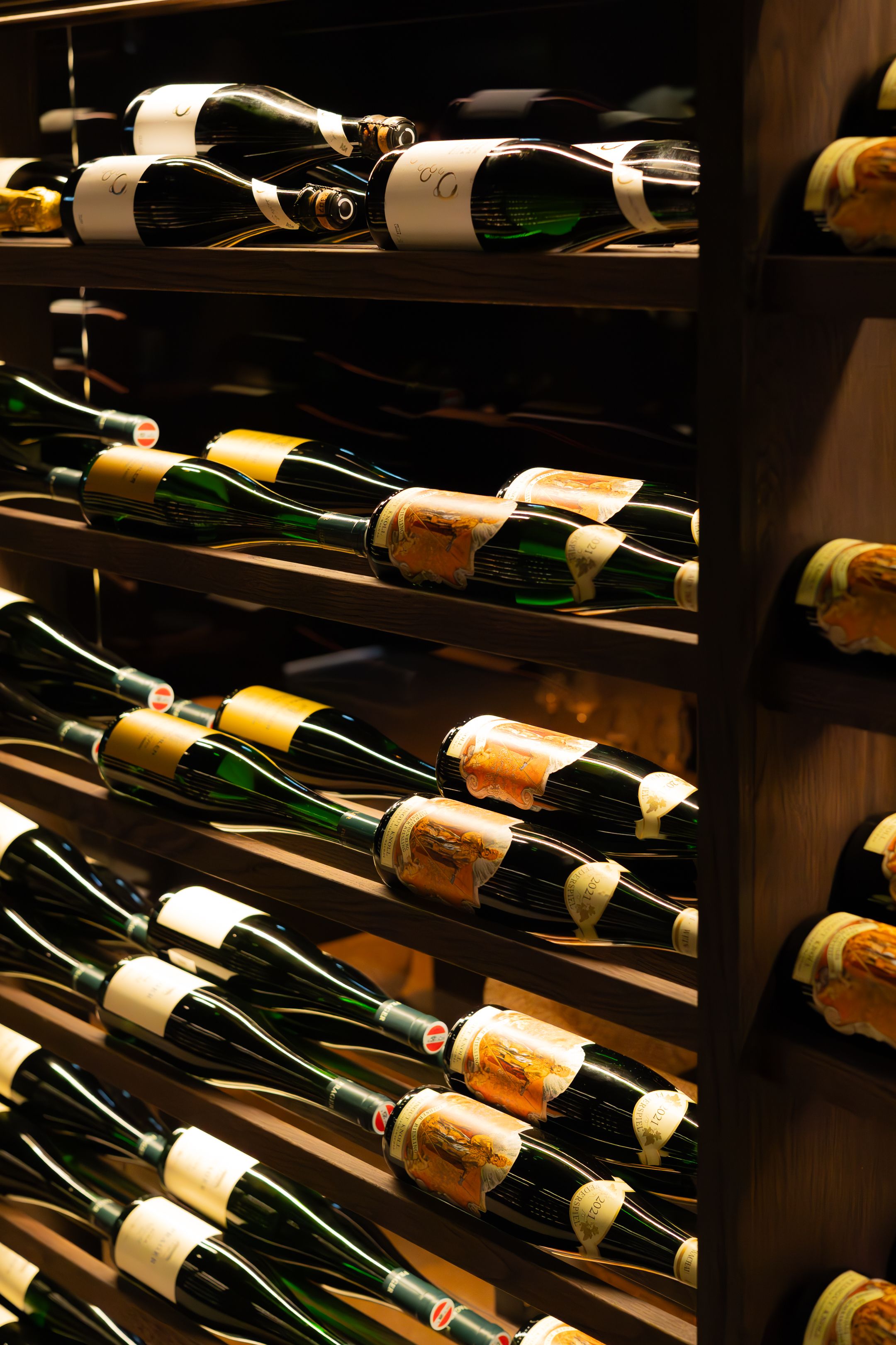 Wine bottles with elegant labels displayed on dark wooden shelves in a cellar.