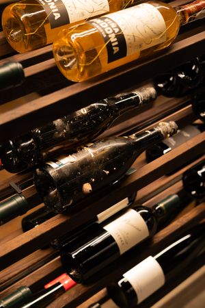 Close-up of vintage wine bottles including golden and dark varieties stored horizontally on wooden racks.