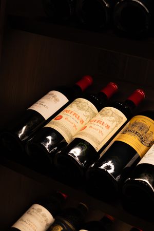Vintage red wine bottles from prestigious vineyards displayed in dark cellar lighting.