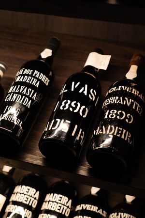 Vintage Madeira wine bottles with black labels displayed on wooden shelving.