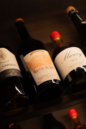 Three fine wine bottles displayed on a dark wooden shelf, showing vintage labels and red wax seals.