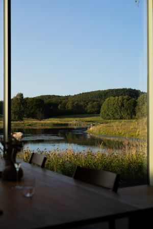 Serene lakeside dining room view with rolling hills and lush greenery in the background.