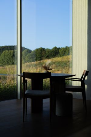 Modern dining table silhouetted against large windows overlooking a scenic natural landscape.