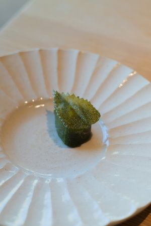 Single green garnish presented on an elegant white fluted plate.