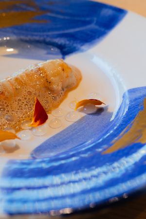 Close-up of a foam-topped dish with red garnish on a blue-swirled ceramic plate.