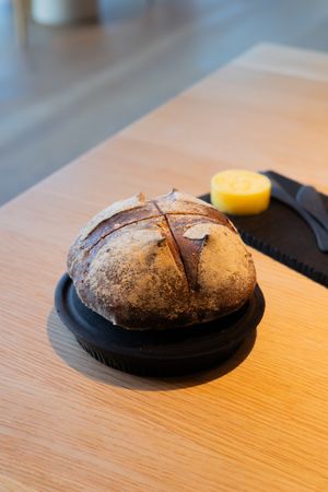 Artisanal dark bread with cross-cut pattern served on a black plate with butter on the side.