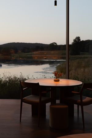 Modern dining table overlooking a serene lake at sunset with pendant lighting creating an intimate atmosphere.