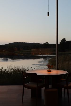 Minimalist dining setup with lake view through large windows at dusk.