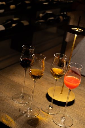 Four elegant stemmed glasses filled with different colored wines on a wooden surface.