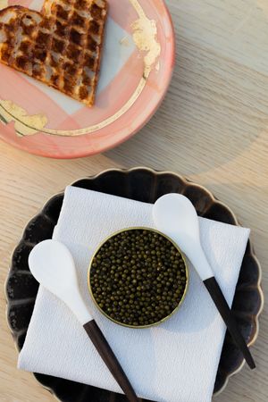 Luxury caviar service with heart waffle on pink plate and black scalloped dish.