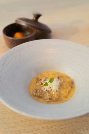 Creamy soup with garnish served in an elegant white bowl on wooden table.