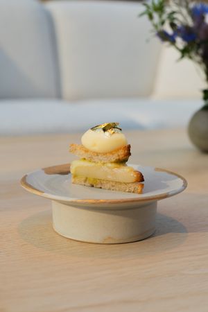 Layered dessert with yellow custard and gold garnish on a ceramic pedestal plate.