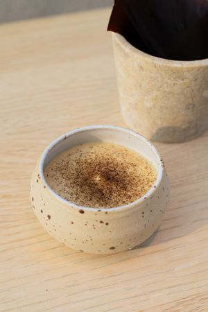 Speckled ceramic bowl containing creamy beverage with dusted spice topping.