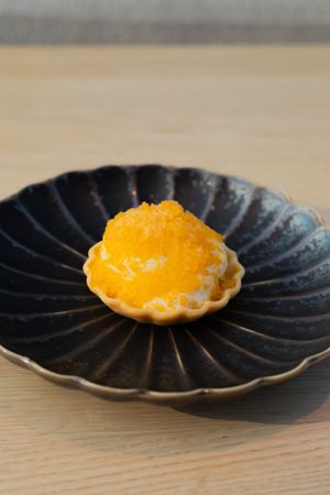 Yellow citrus tart on a black fluted ceramic plate with decorative edges.