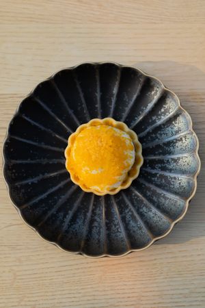 Bright yellow custard tart centered on black fluted ceramic plate.