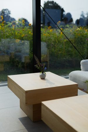 Minimalist wooden coffee table with small vase against window overlooking yellow wildflower field.