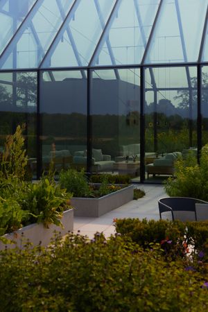 Modern glass conservatory with outdoor seating area surrounded by lush garden landscaping.