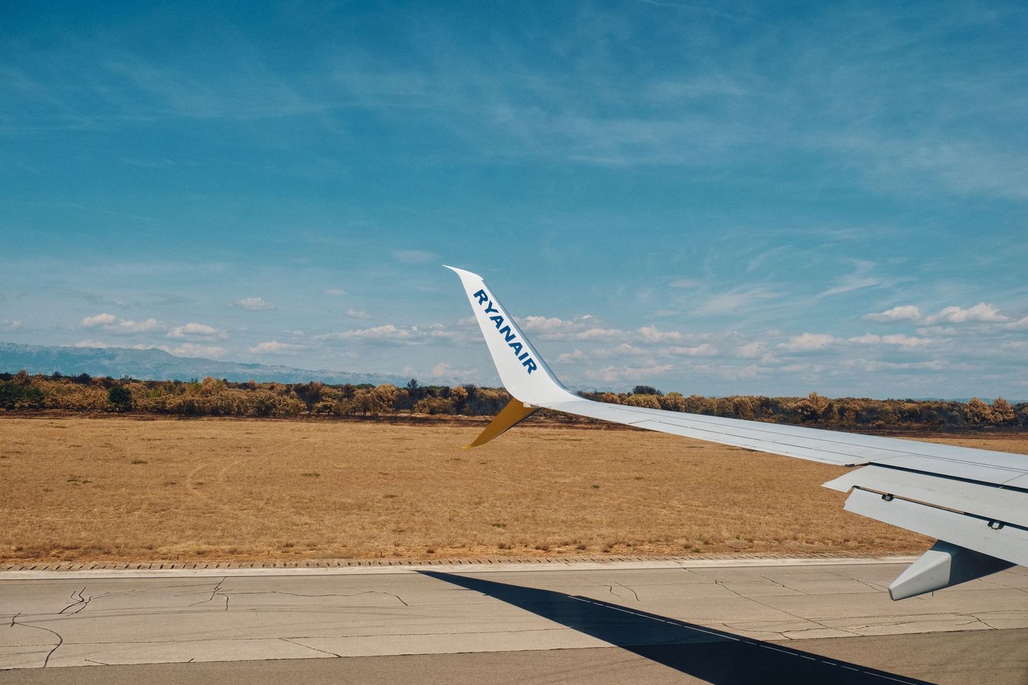 Aircraft wing view over desert landscape against bright blue sky.