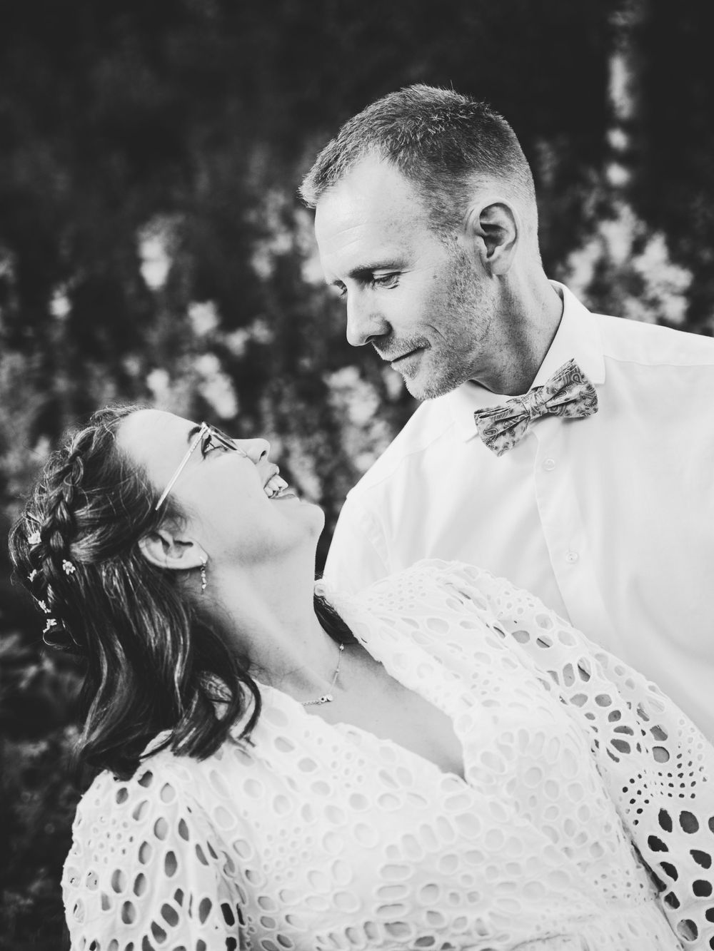 Black and white portrait of a bride and groom sharing an intimate moment outdoors with the bride tilting back in laughter.