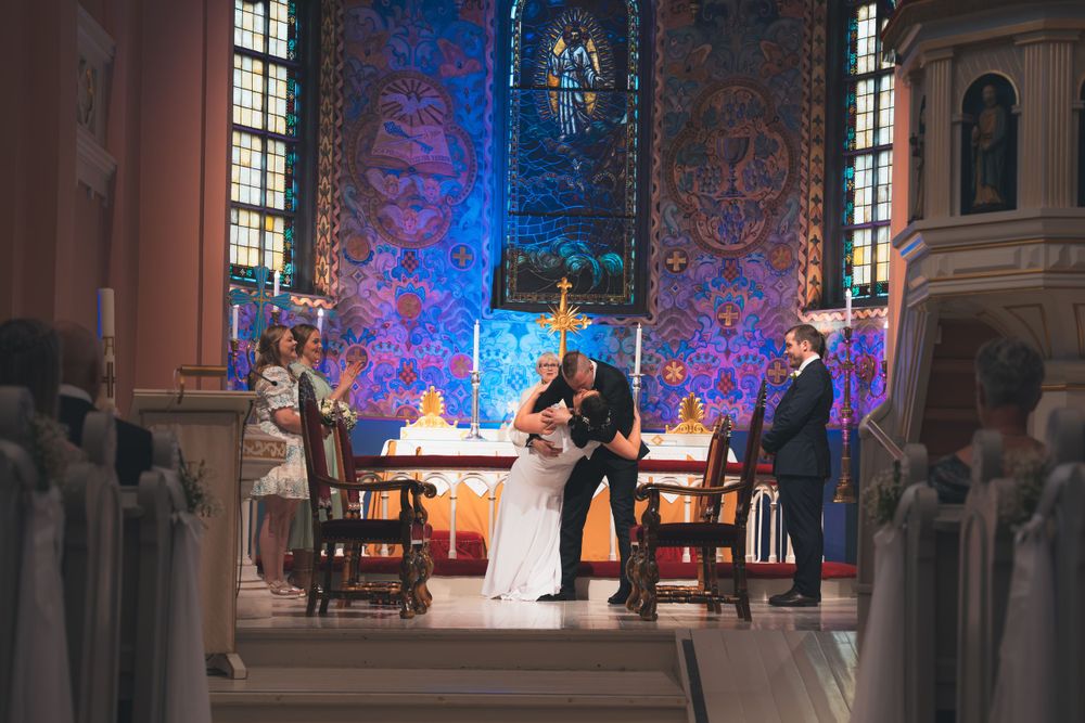 Wedding ceremony takes place in historic church with dramatic blue lighting and ornate architectural details.