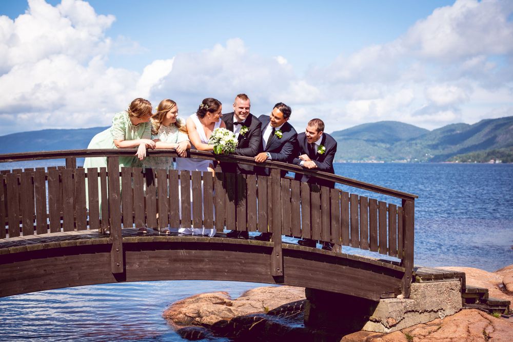Wedding party gathered on wooden bridge overlooking scenic mountain lake view.
