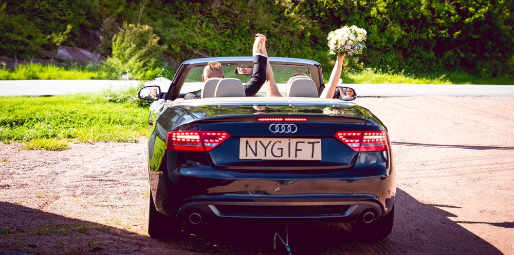 Black Audi convertible decorated as wedding getaway car with bouquet raised through sunroof.