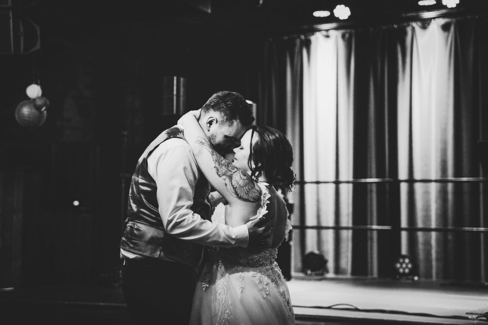 Black and white photo of a bride and groom sharing a romantic first dance kiss at their wedding reception.