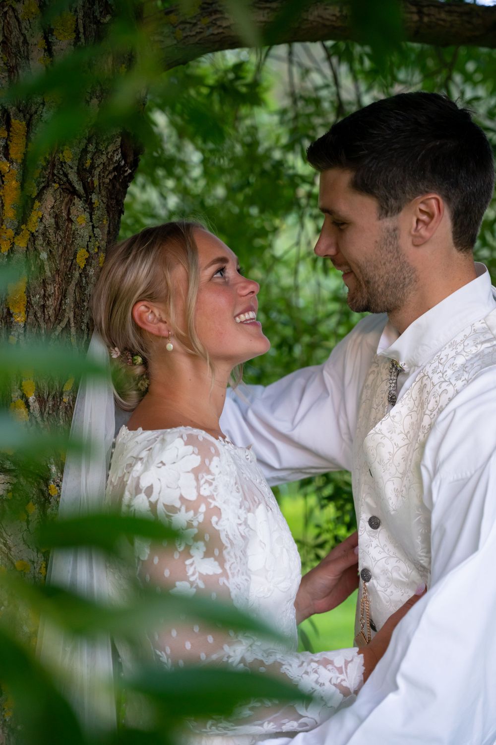 Romantic wedding portrait through green foliage with lace dress details.