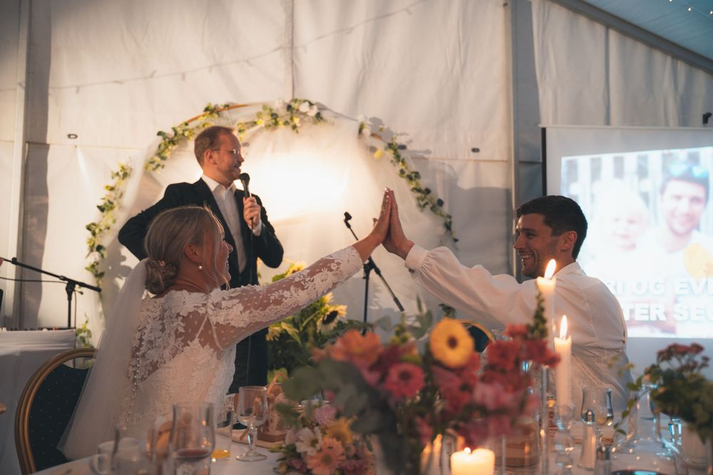 A wedding reception celebration under a floral arch with guests toasting in an indoor venue.