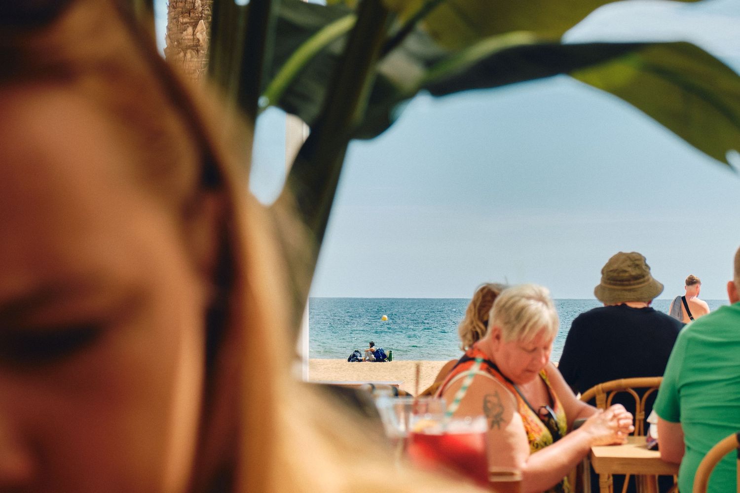 Beachfront restaurant terrace with diners enjoying ocean views on a sunny afternoon.