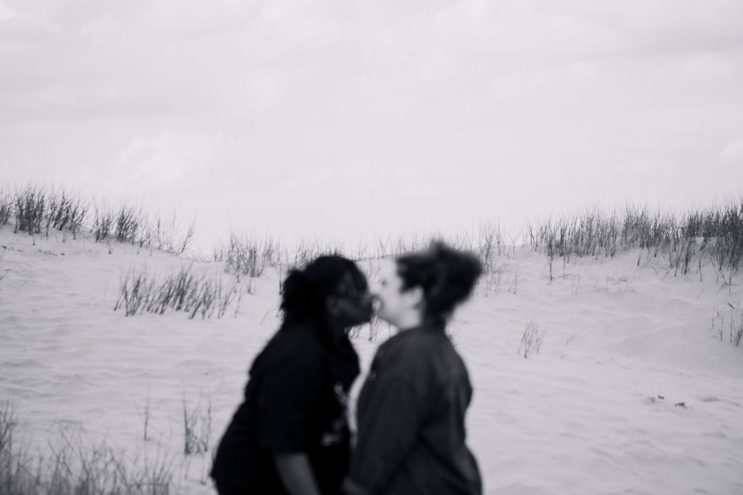 A tender moment captured in the dunes — a soft, blurred kiss, timeless and intimate. LGBTQ+