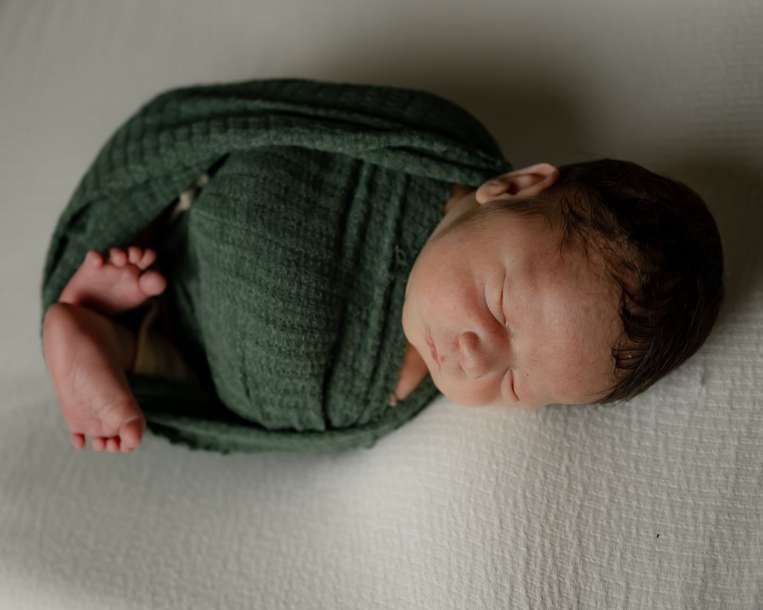 Peaceful newborn baby sleeping while wrapped in soft green swaddling fabric.