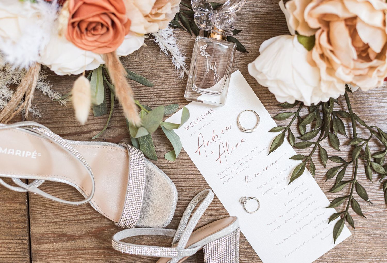 A flat lay portrait of the details of a wedding day including the rings, flowers, bride's shoes, and invitation.