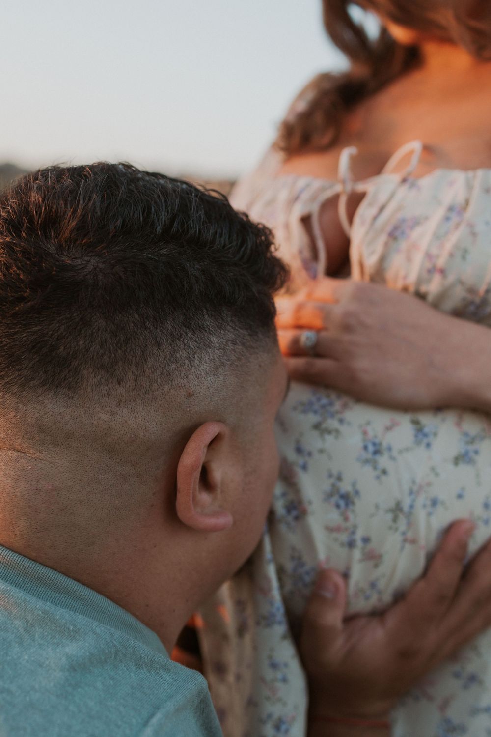 Close-up side view of a couple embracing while wearing casual clothing in soft lighting.