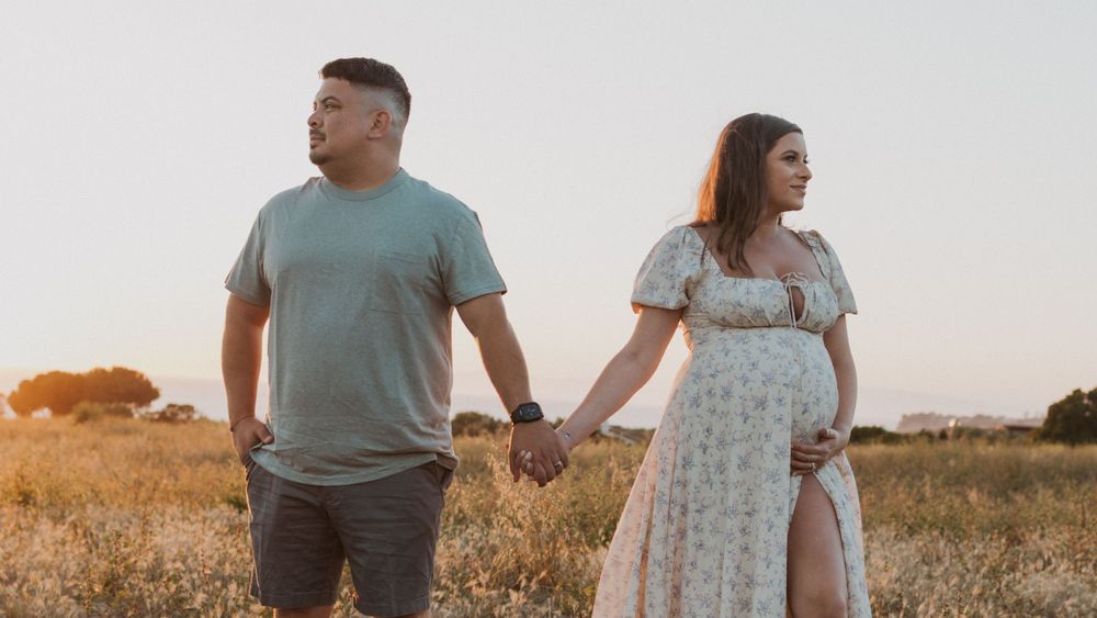 A couple holds hands while standing in a golden field at sunset.
