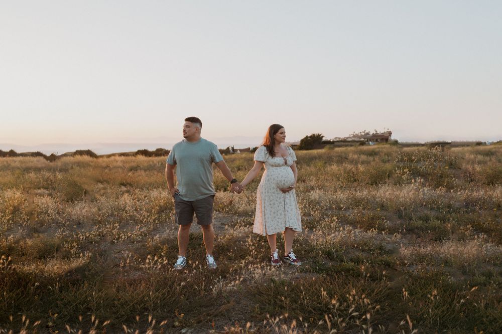 A couple stands together in a field during sunset.