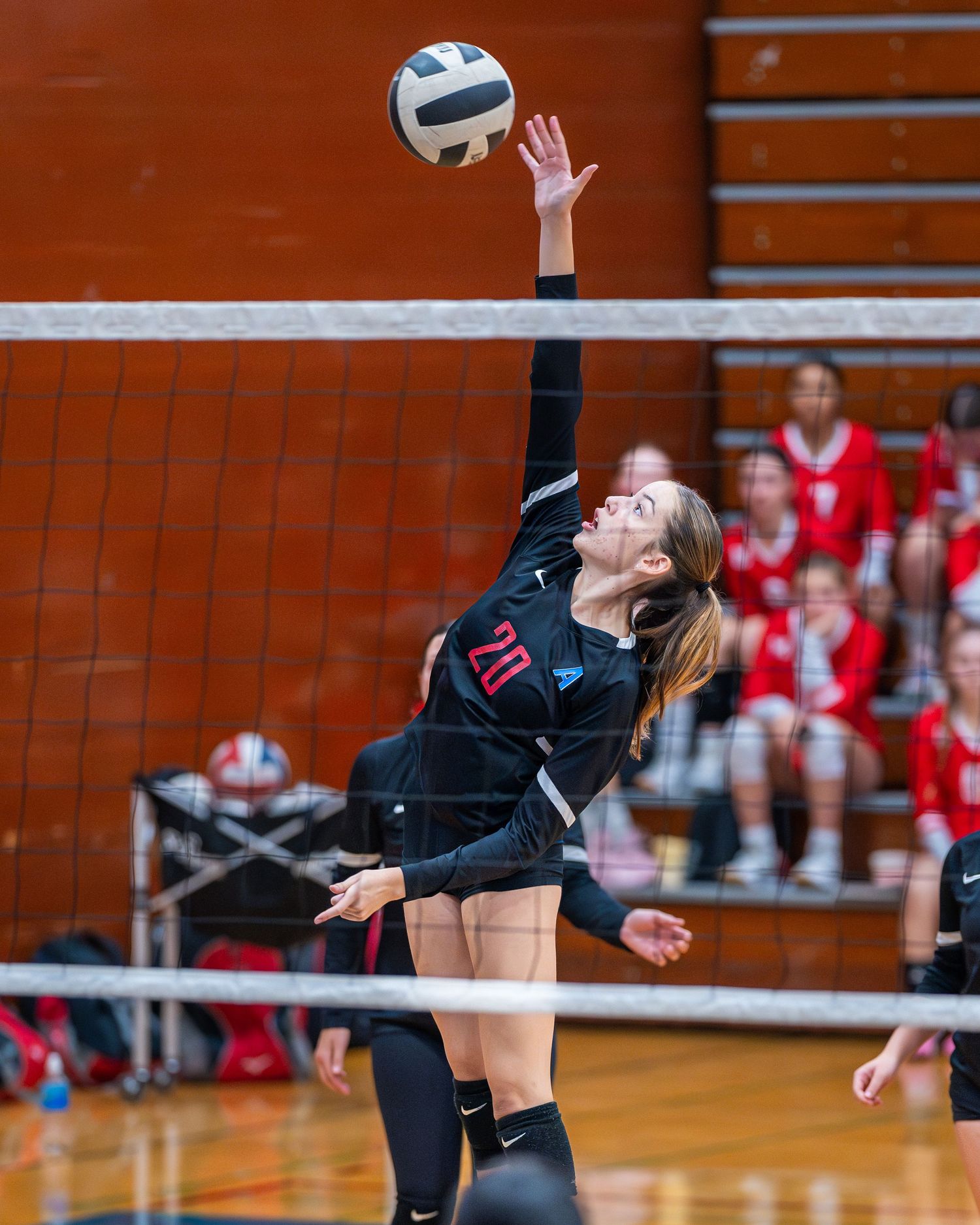 Indoor volleyball player jumping to spike ball over net during intense match.