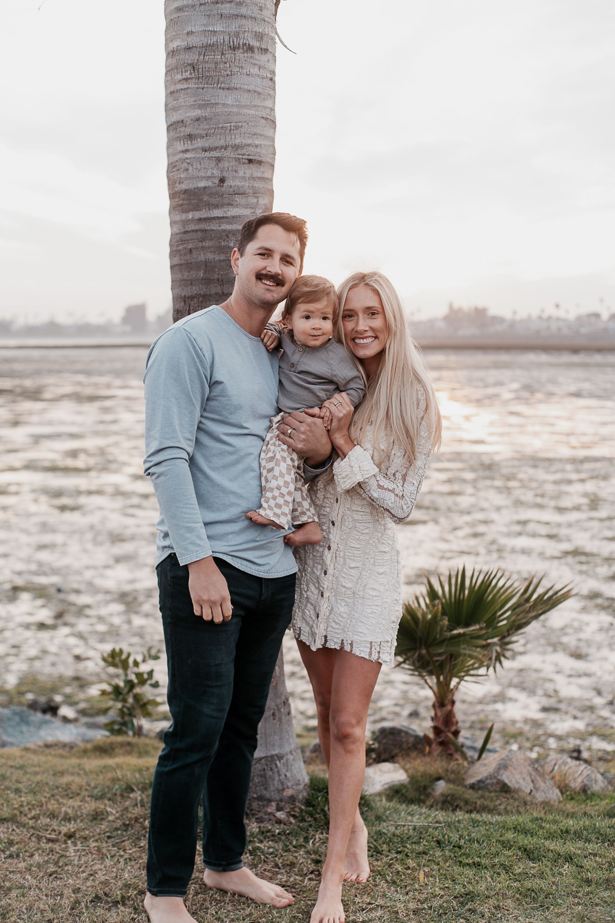 Family moment captured under palm tree near rocky coastline.