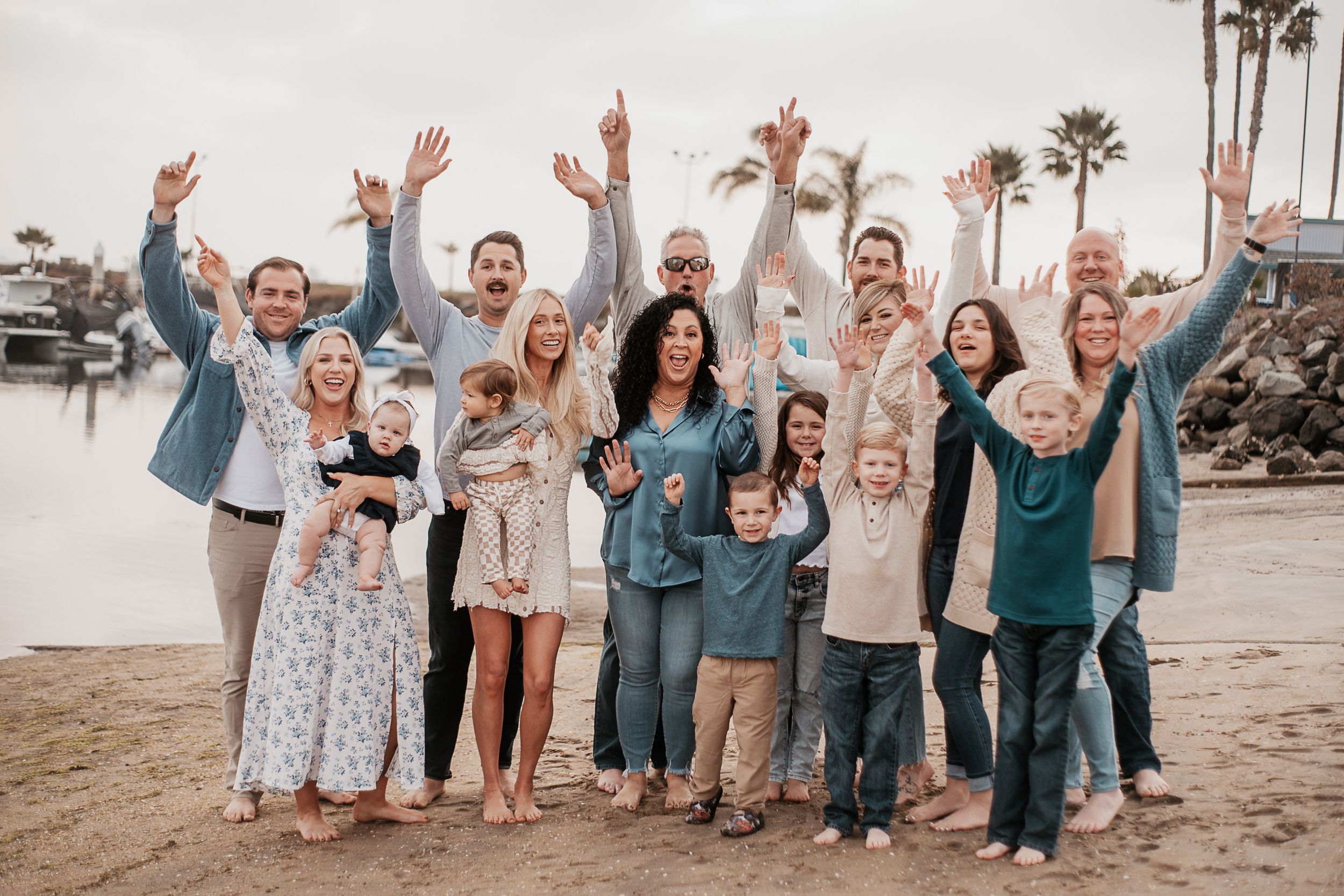 A large family group poses together on the beach with raised arms.