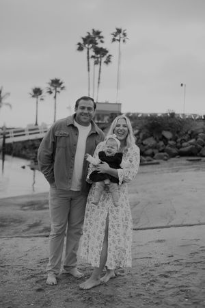 A family portrait on a cloudy beach day with palm trees in the background.