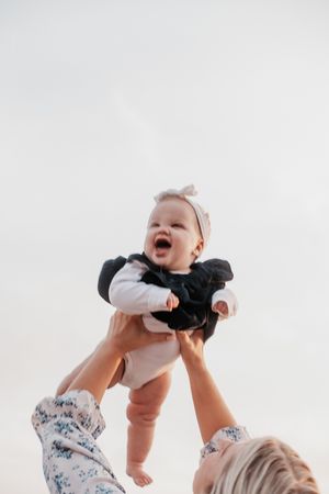 Baby being lifted joyfully into the air against cloudy sky.