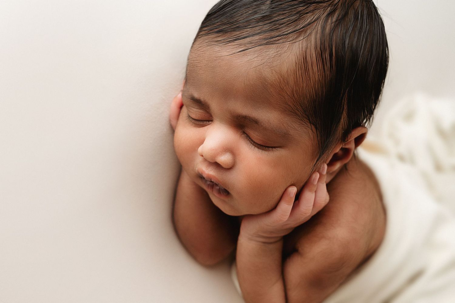 Sleepy newborn resting on white textured backdrop during professional photo session.