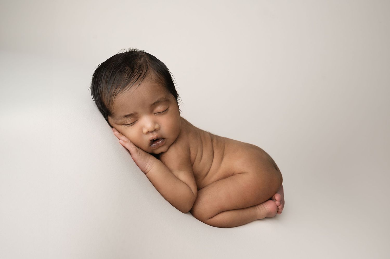 Side profile of sleeping newborn on minimalist gray studio backdrop.