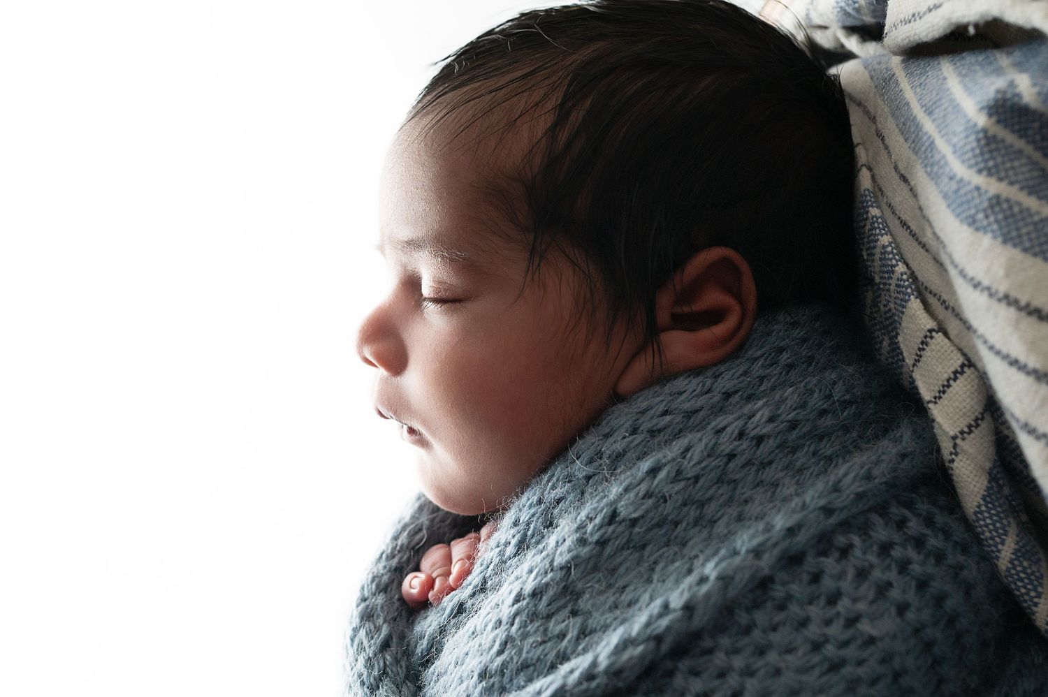 Sleeping newborn baby swaddled in cozy gray knit wrap against blue backdrop.