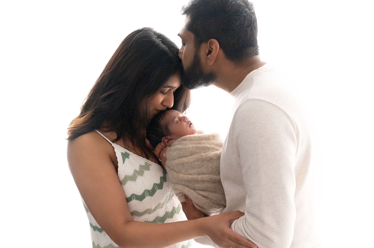 Parents embracing while holding their newborn in casual studio portrait.