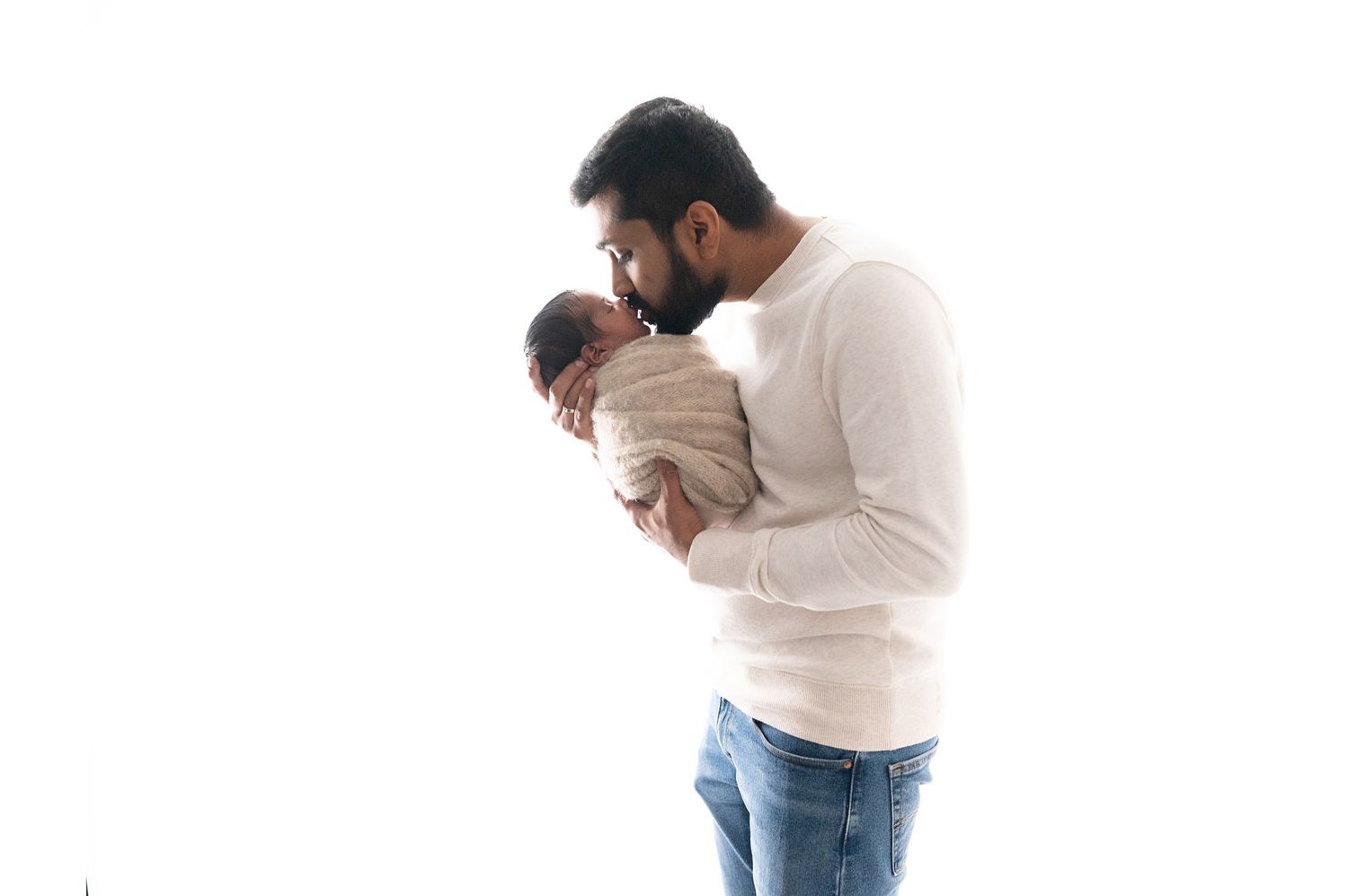 Parents in white and jeans sharing tender moment in bright studio setting.