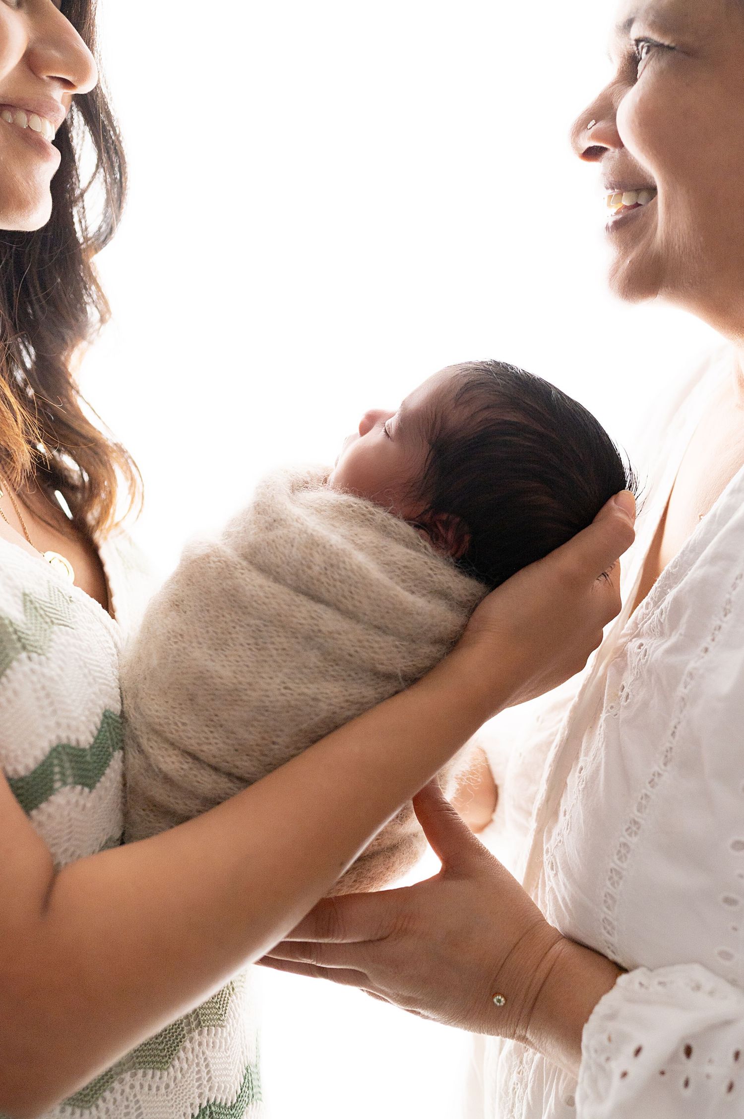 Parents holding newborn wrapped in beige blanket against white background.