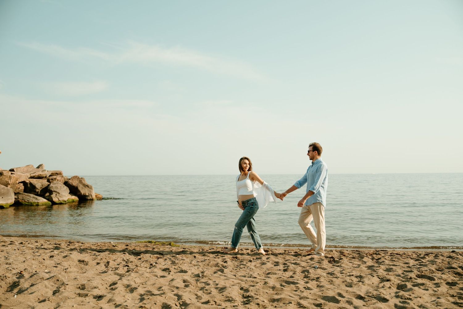 Playful couple holding hands while dancing on sandy beach by ocean.