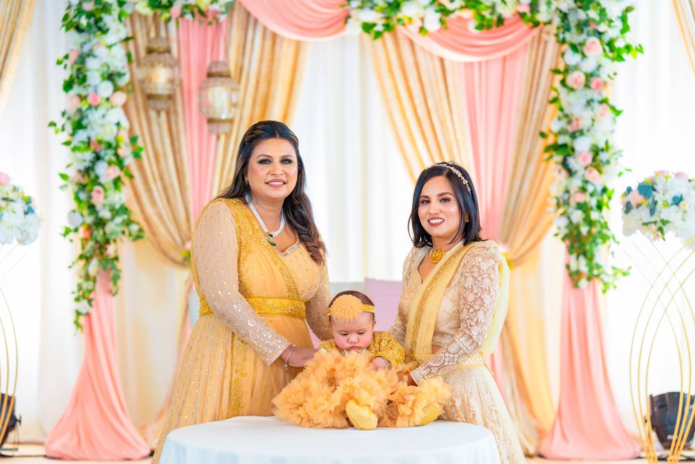 Three people in yellow and gold outfits pose against floral decorated backdrop.