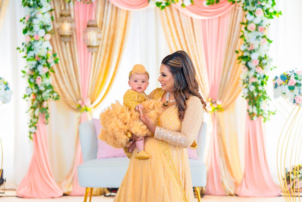 Mother holds baby in coordinating yellow outfits against elegant draped backdrop.